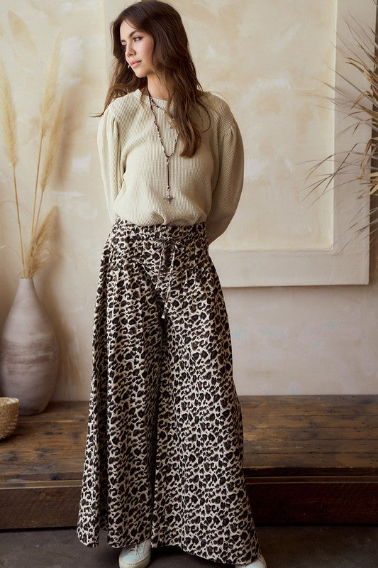 Front view — leopard print wide-leg pants with high rise and tie waist, flowy woven drape; styled with a beige knit sweater on model.
