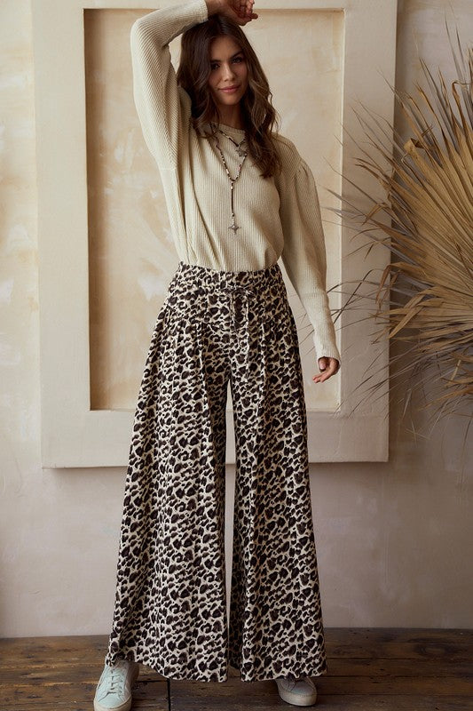 Front view — leopard print wide-leg pants with high rise and tie waist, flowy woven drape; styled with a beige knit sweater on model.