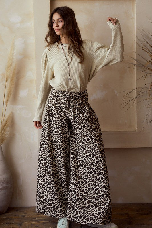 Front view — leopard print wide-leg pants with high rise and tie waist, flowy woven drape; styled with a beige knit sweater on model.
