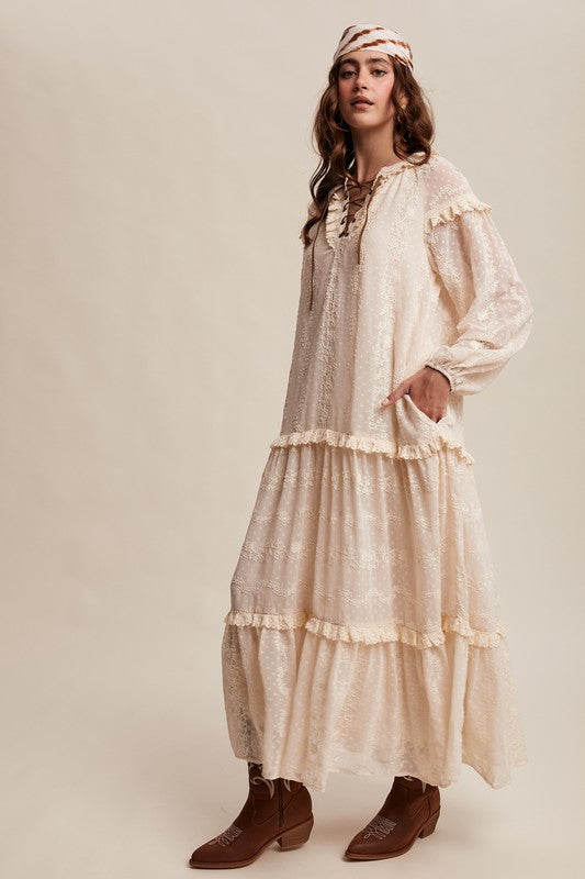 Model in ivory boho maxi dress with lace-up neckline, long puff sleeves, and tiered ruffle skirt, styled with concho belt, headscarf, and western boots.