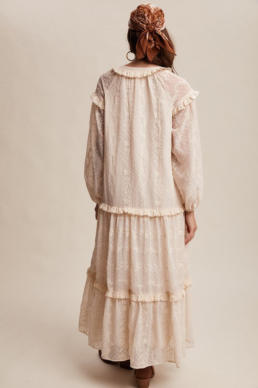 Back view of model in an ivory boho maxi dress with long sleeves, ruffled trim, and tiered skirt, styled with a brown headscarf and ankle boots.