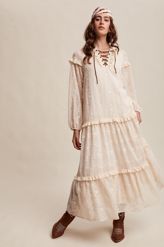 Model in ivory boho maxi dress with lace-up neckline, long puff sleeves, and tiered ruffle skirt, styled with concho belt, headscarf, and western boots.