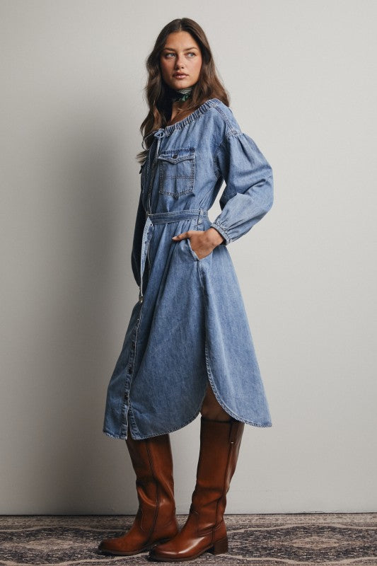 Woman wearing a blue denim dress and brown knee-high boots against a plain background