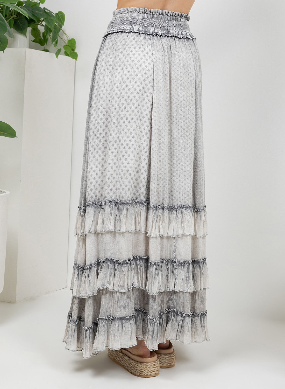 A tiered maxi skirt with a light gray and white polka dot pattern, featuring an elastic waistband and multiple ruffled layers, shown on a model wearing espadrille sandals.