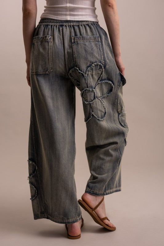 Back view of wide leg flower patchwork denim pants with elastic waistband and raw-edge daisy cutout detail