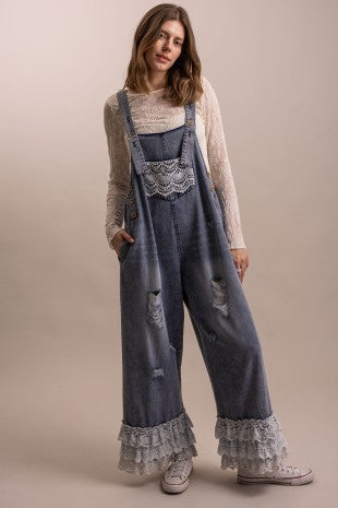 Full length front view of distressed denim overall with crochet lace bib pocket, wide leg silhouette, and tiered lace ruffle hem