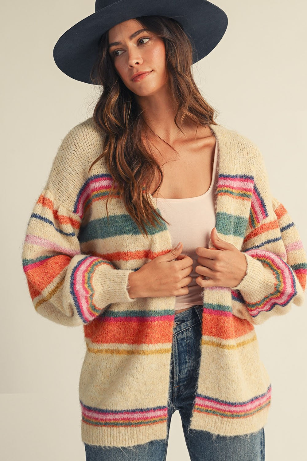 Woman wearing a colorful striped cardigan and navy hat against a plain background