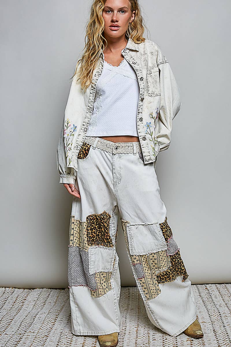 Woman wearing a stylish outfit with a jacket and patchwork pants against a plain background