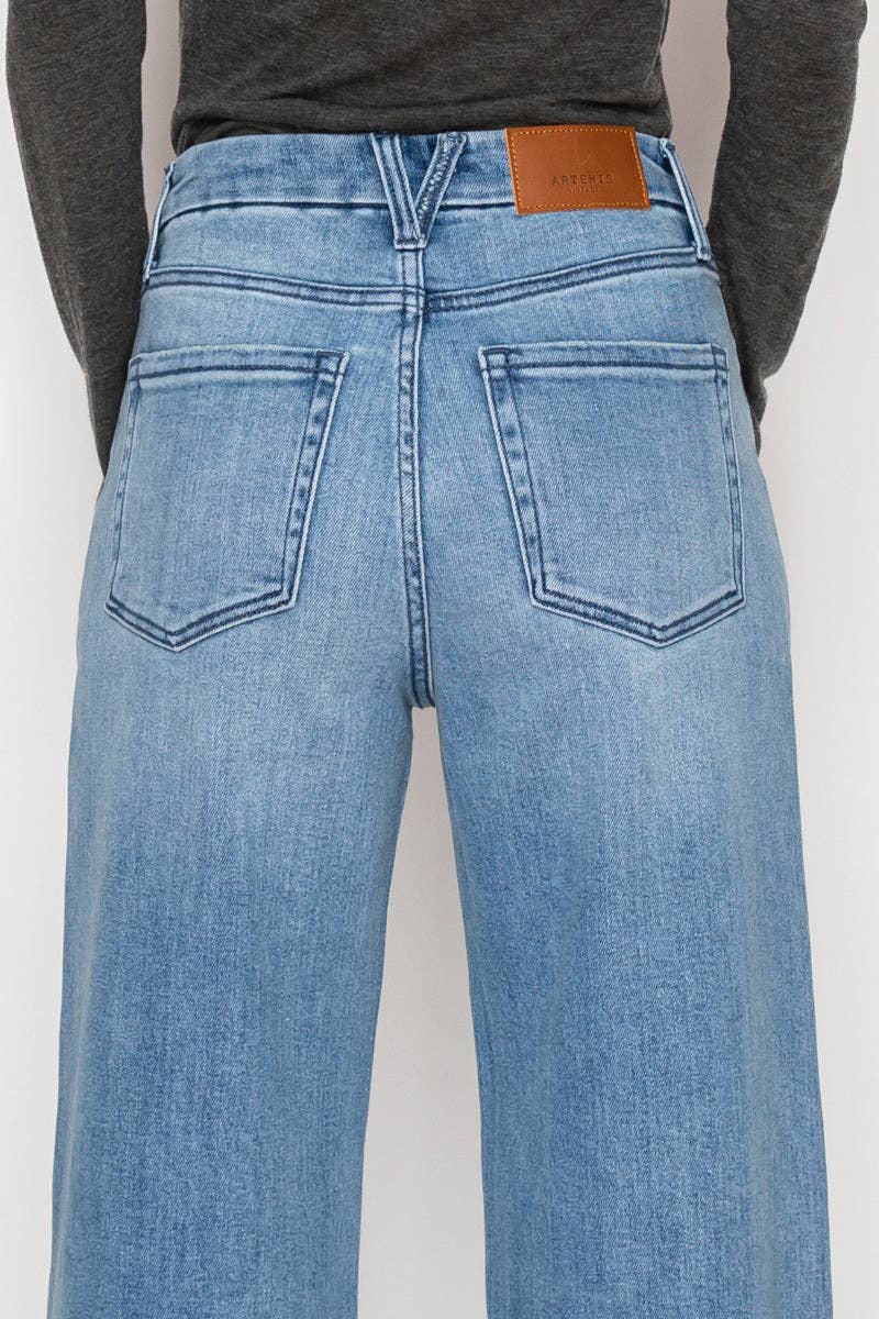 Close up rear view of model wearing ultra high-rise wide-leg jeans in medium stone wash with cuff detail and button accents along the leg