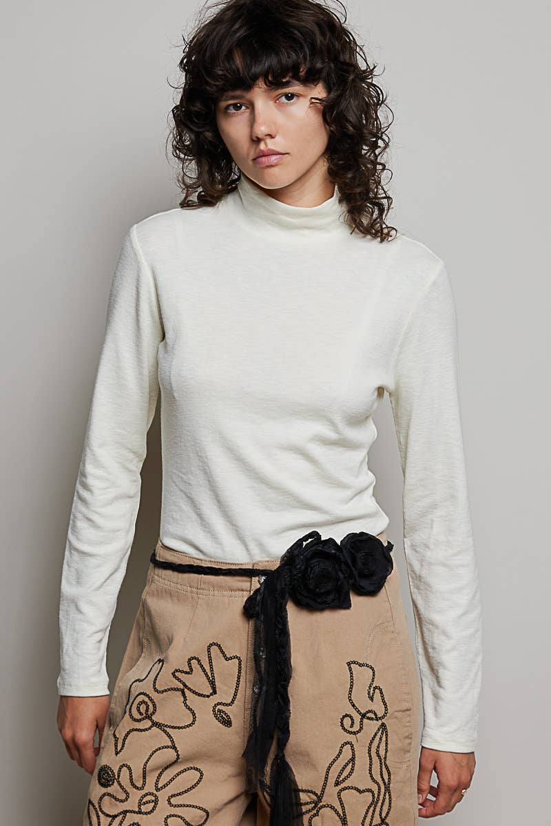 Person wearing a white turtleneck and beige skirt with floral patterns against a plain background