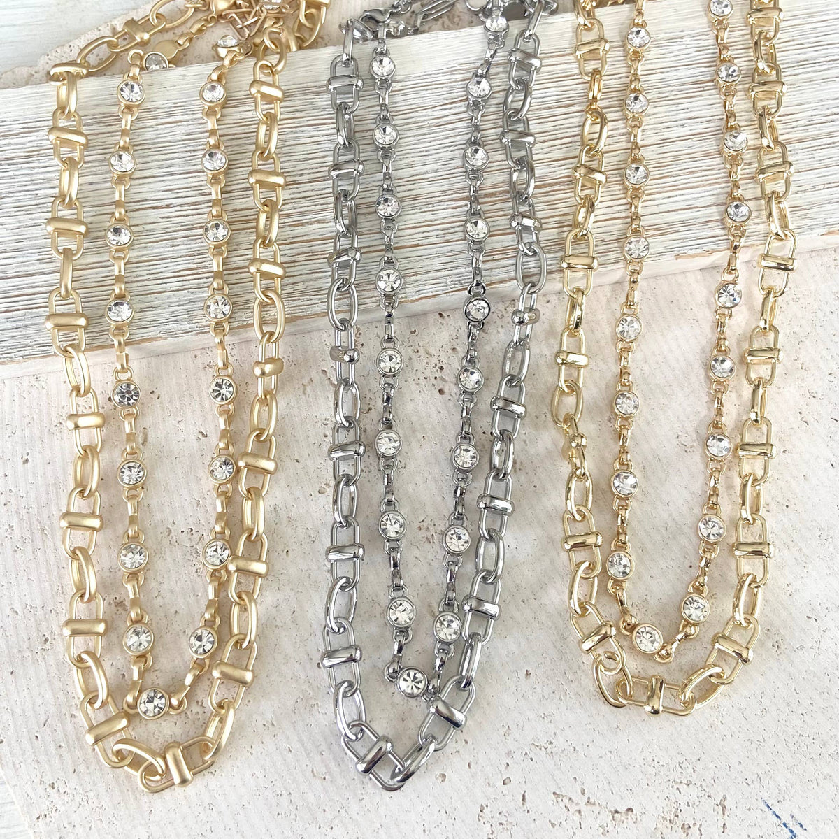 Three chain necklaces in gold, silver, and a combination of both on a textured surface.