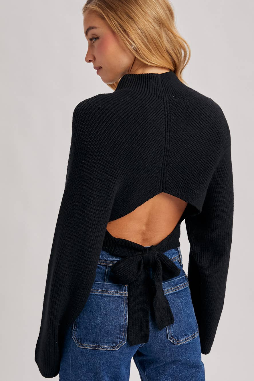 Black open-back knit sweater with long sleeves and waist-tie bow, styled with high-rise blue jeans.