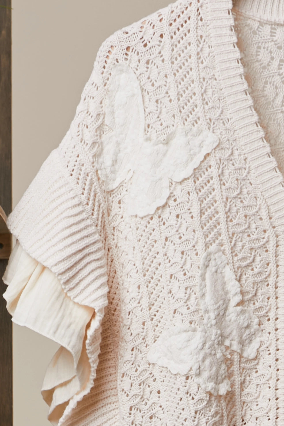 Close-up of Butterfly Bloom Cardigan cream-colored open-knit cardigan featuring textured lace patterns and layered 3D butterfly appliqués, paired with a matching ruffled blouse.