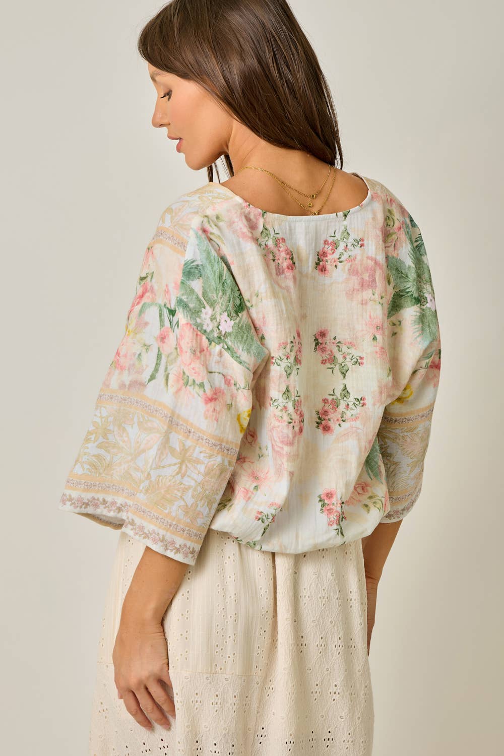 Woman wearing a floral blouse and light-colored pants against a neutral background