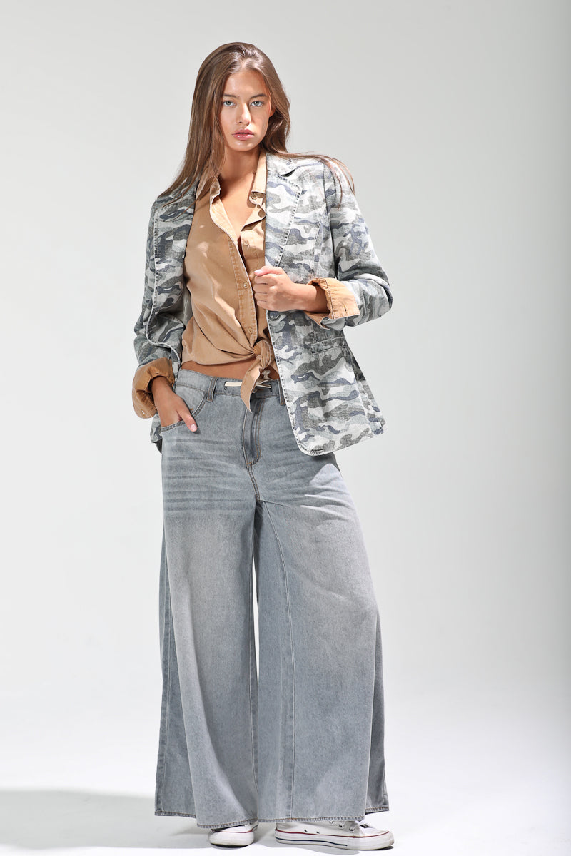Model wearing camo print single-breasted blazer styled with tan button-up shirt and wide-leg gray denim trousers, front view.