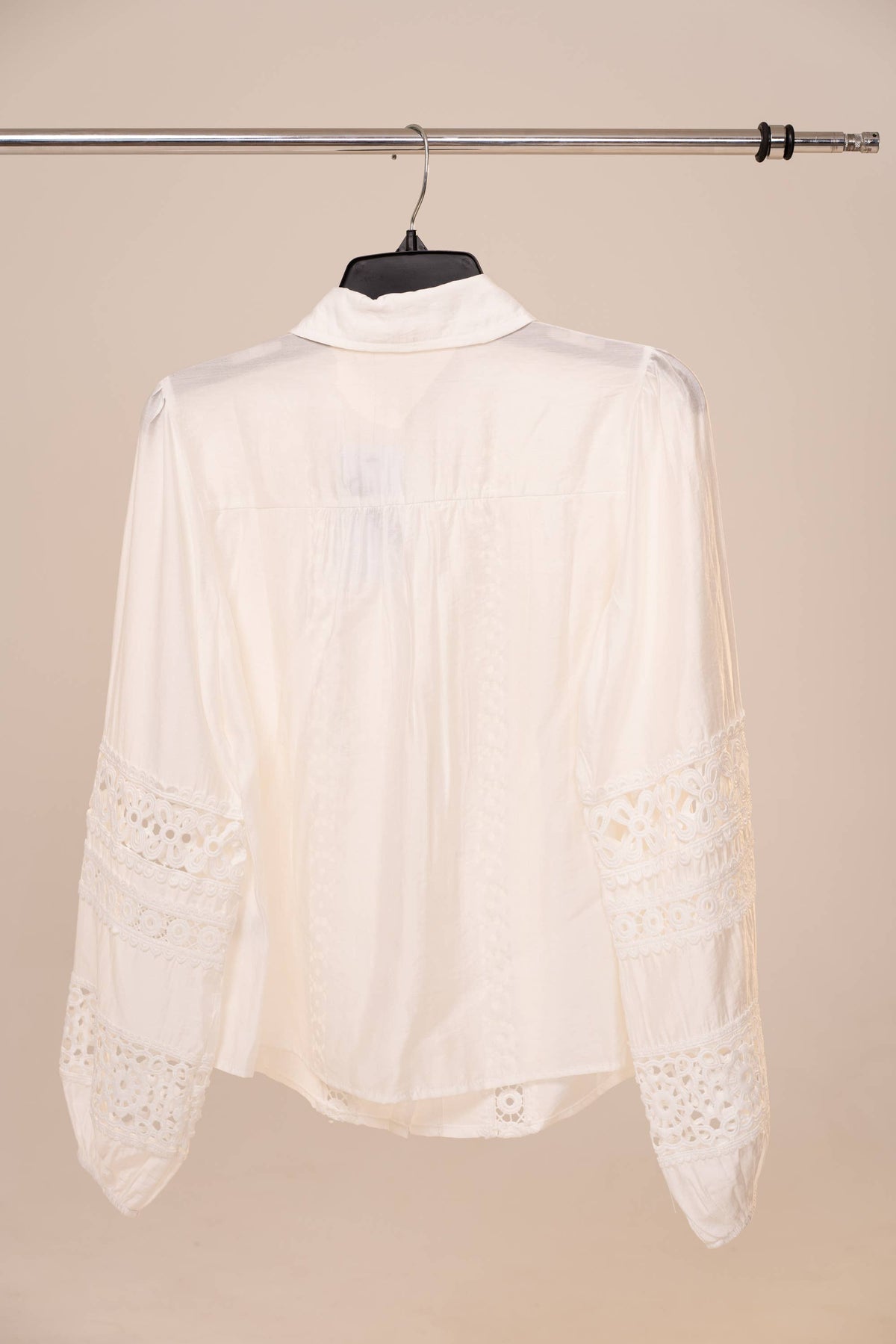 White lace blouse on a hanger against a beige background