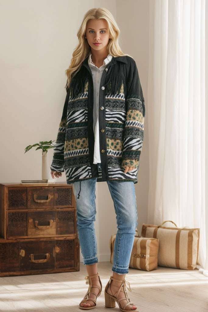 Brown Aztec print shacket with fringe detail, button closure, and patterned sleeves, styled with cream pleated pants while seated on a sofa.