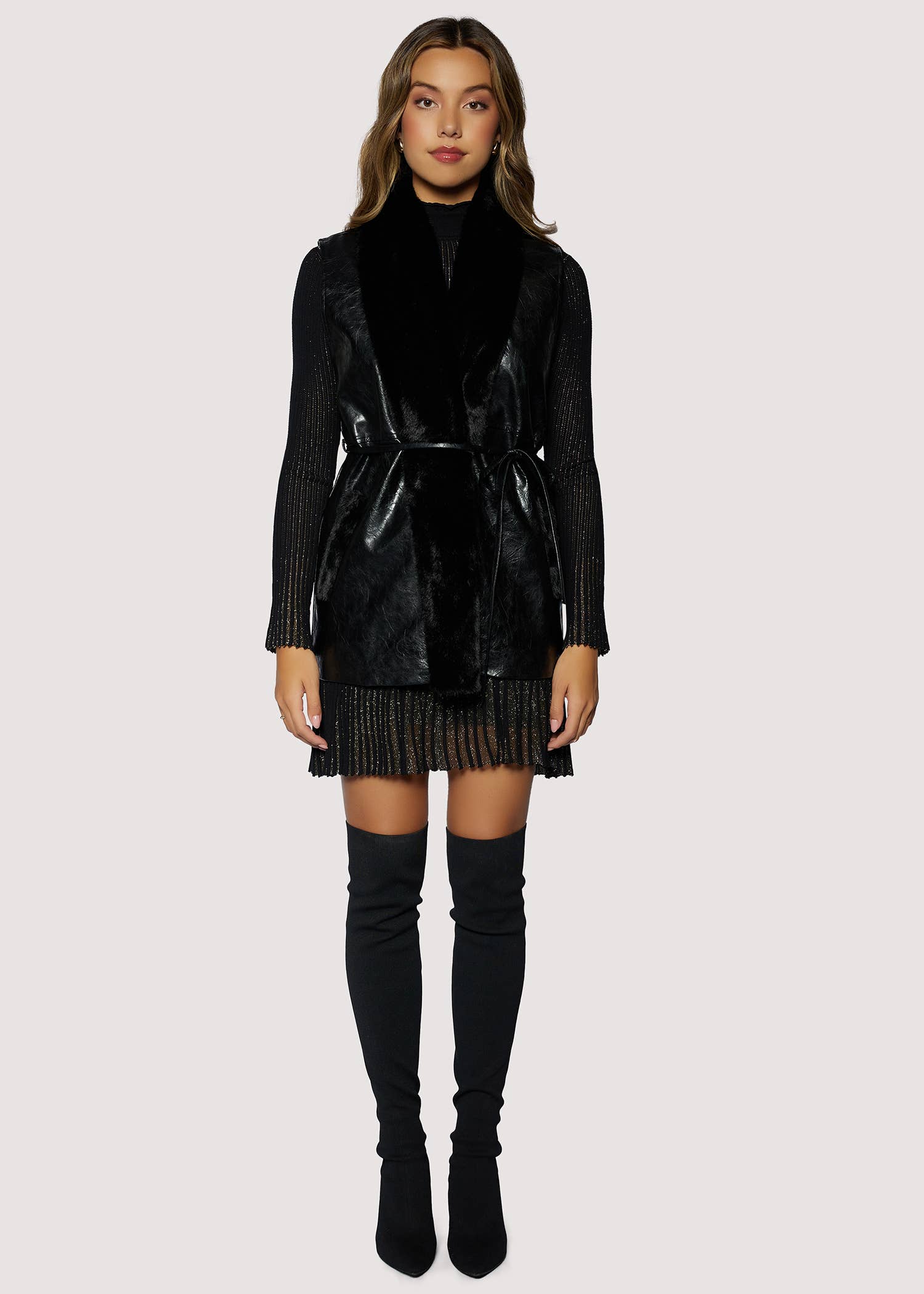 Woman wearing a black leather jacket, black turtleneck, and black skirt with knee-high boots on a white background