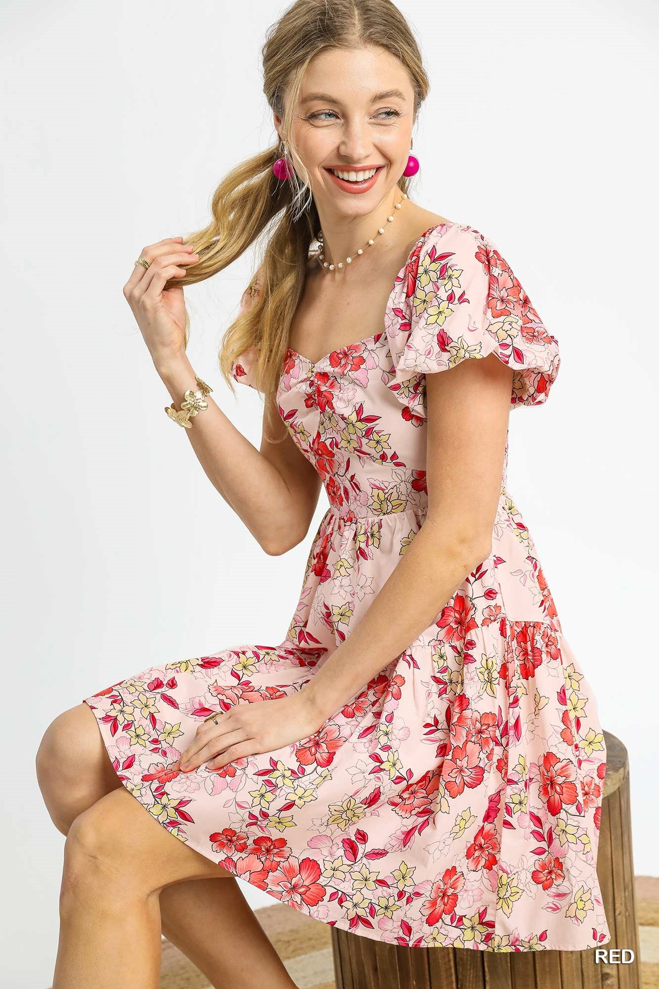 Woman wearing a floral dress sitting on a wooden stool against a white background
