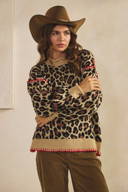 Leopard print knit sweater in tan with ribbed crew neck, cuffs and hem and red whipstitch trim, styled with brown corduroy pants and a cowboy hat.