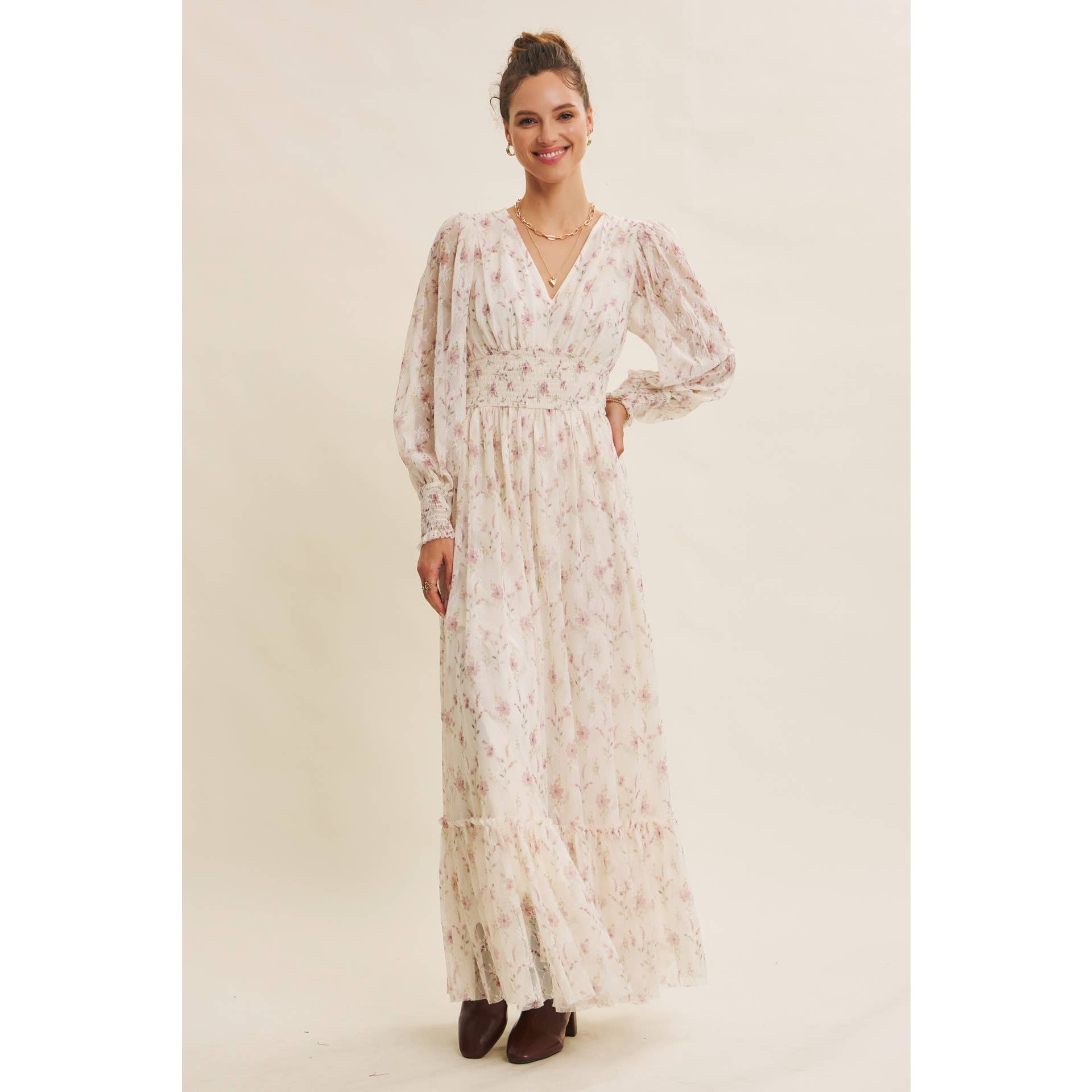 Front view — cream floral chiffon maxi dress with V-neck, sheer long sleeves, smocked waist, and ruffle hem; styled with brown boots.