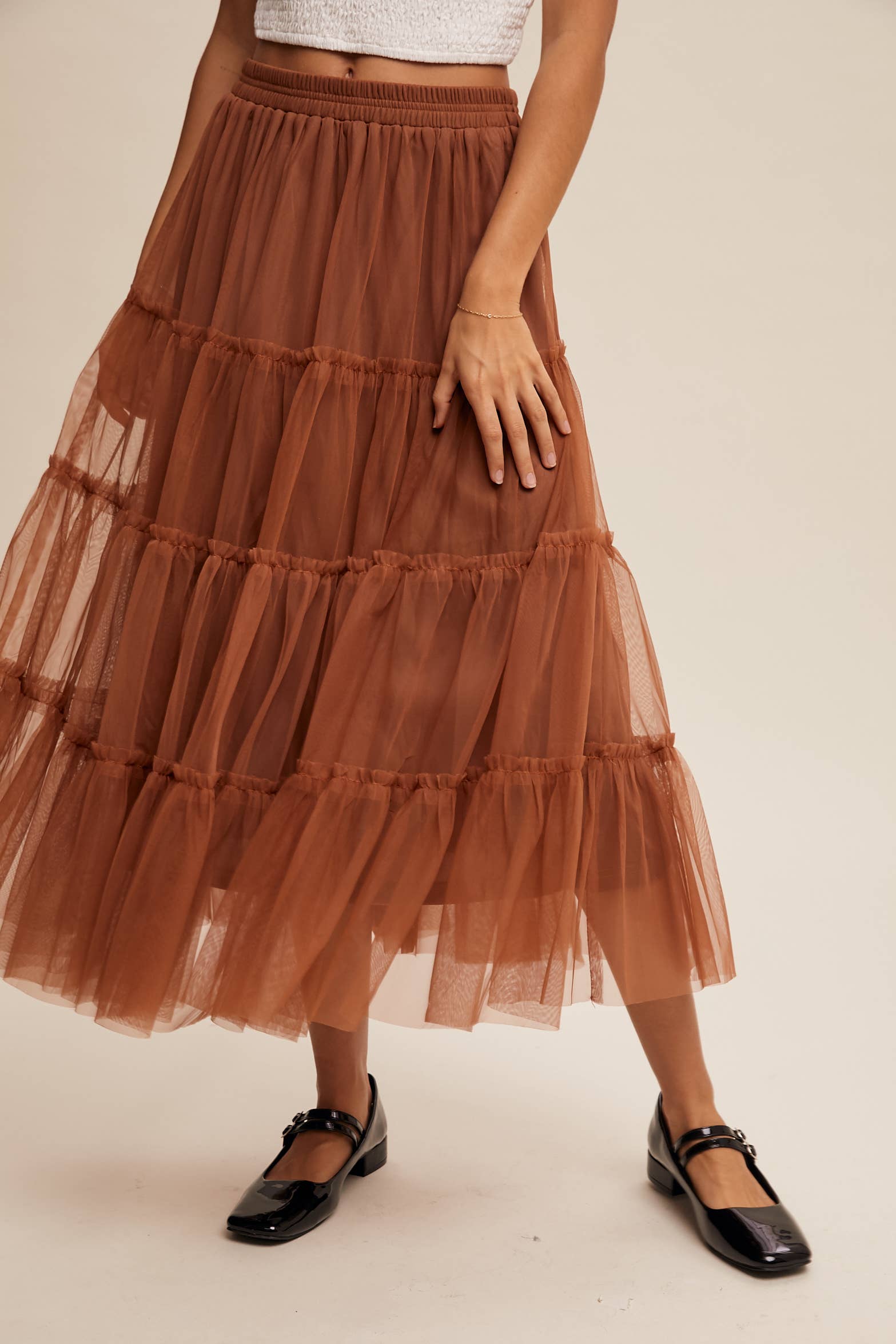Close-up — rust tulle tiered midi skirt with elastic waist and ruffled layers, sheer overlay, styled with black Mary Jane flats.