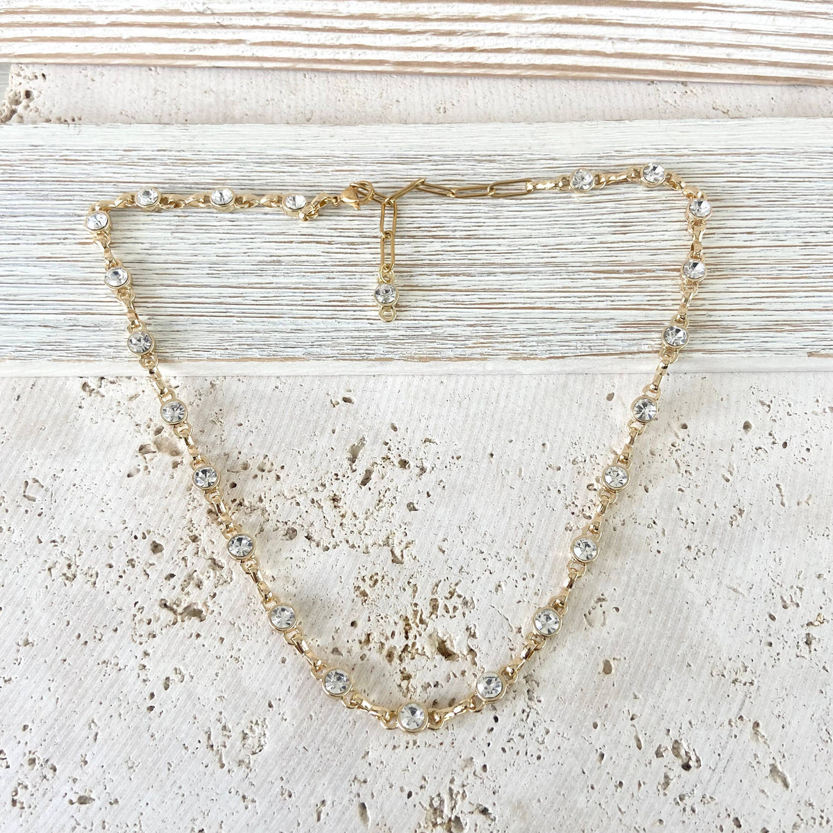 Gold necklace with small crystals on a textured beige surface