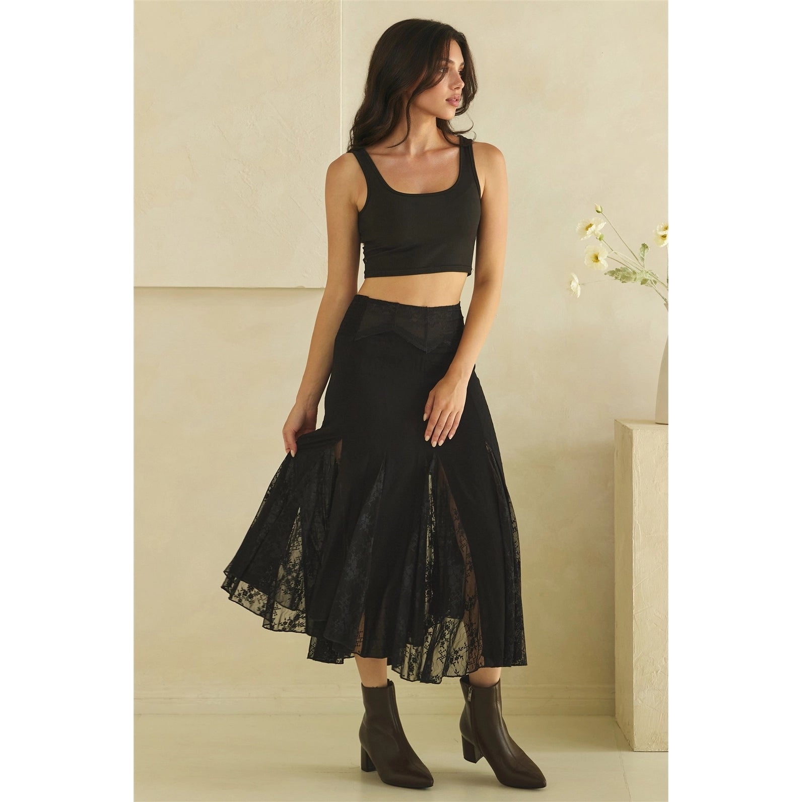 Calla Lace Godet Maxi Skirt in Black by Oli & Hali — three-quarter front view showing flowy black satin and lace godet panels with asymmetric handkerchief hem, styled with black crop top and ankle boots