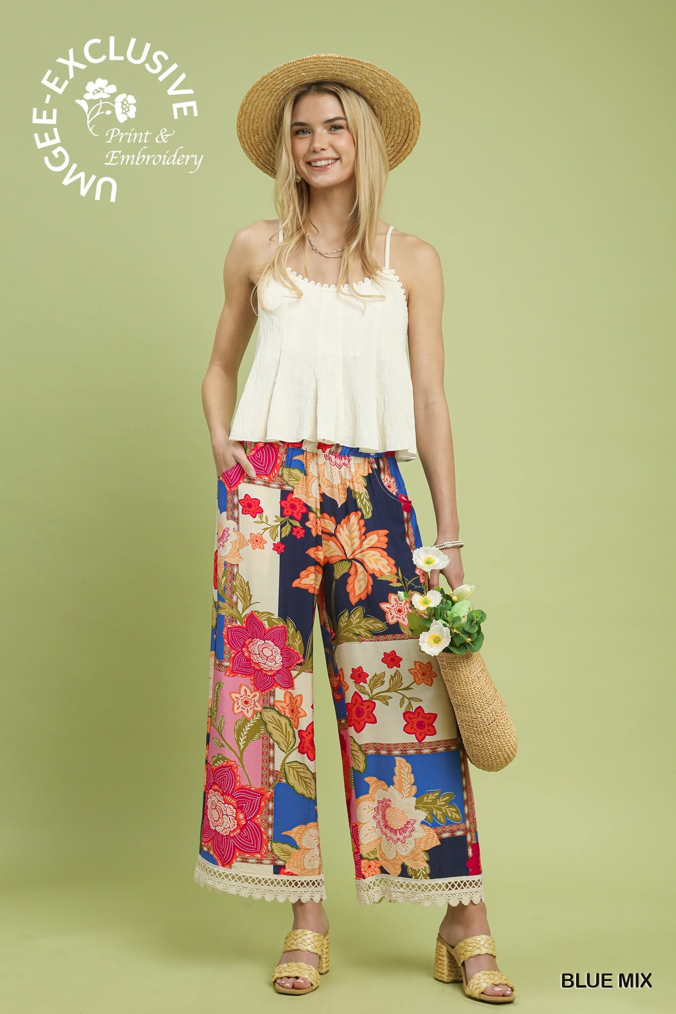 Woman wearing a white top and colorful floral pants on a green background with Umgee branding.