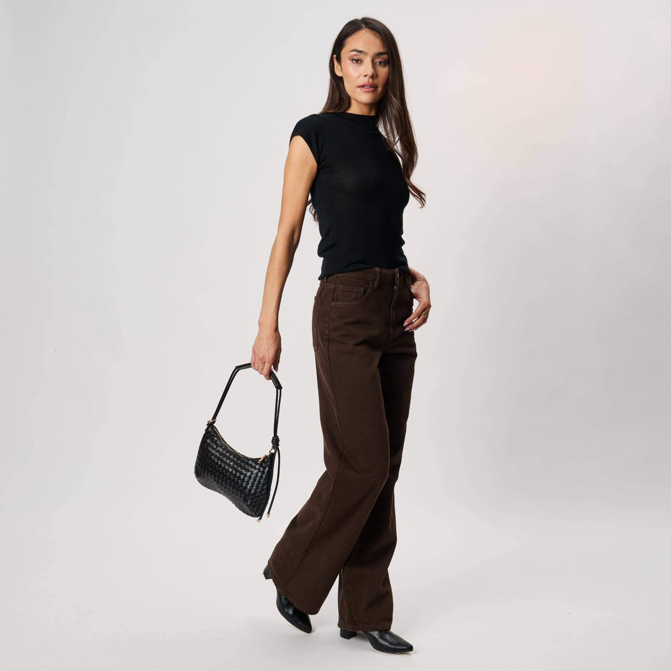 Cindy Woven Crescent Shoulder Bag Black by Moda Luxe A woman modeling a black sleeveless top and dark brown wide-leg pants, holding a black croc-embossed shoulder bag against a light gray studio background.