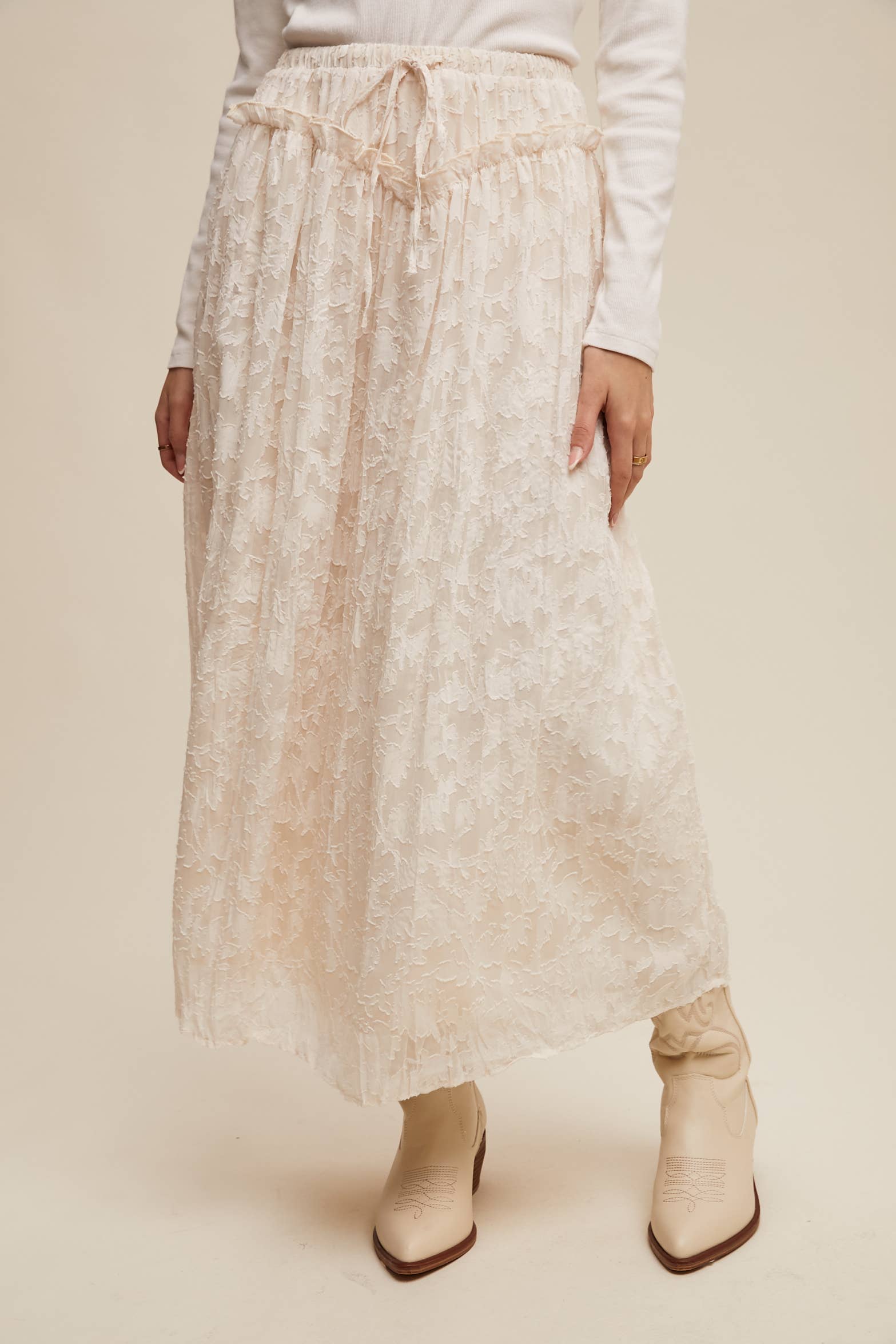 Ivory floral lace maxi skirt with elastic drawstring waist and ruffle detail, ankle-length bubble hem; shown on model with cream western boots.