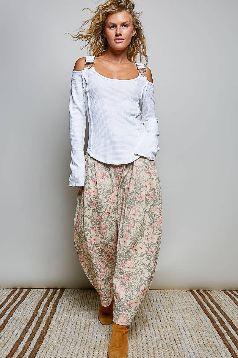 Woman wearing a white top and floral pants against a plain background
