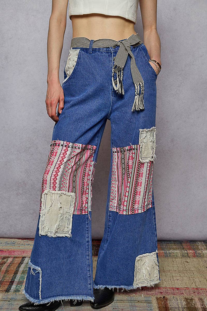 black and cream striped woven belt with braided fringe tassels tied at the waist of blue denim jeans.