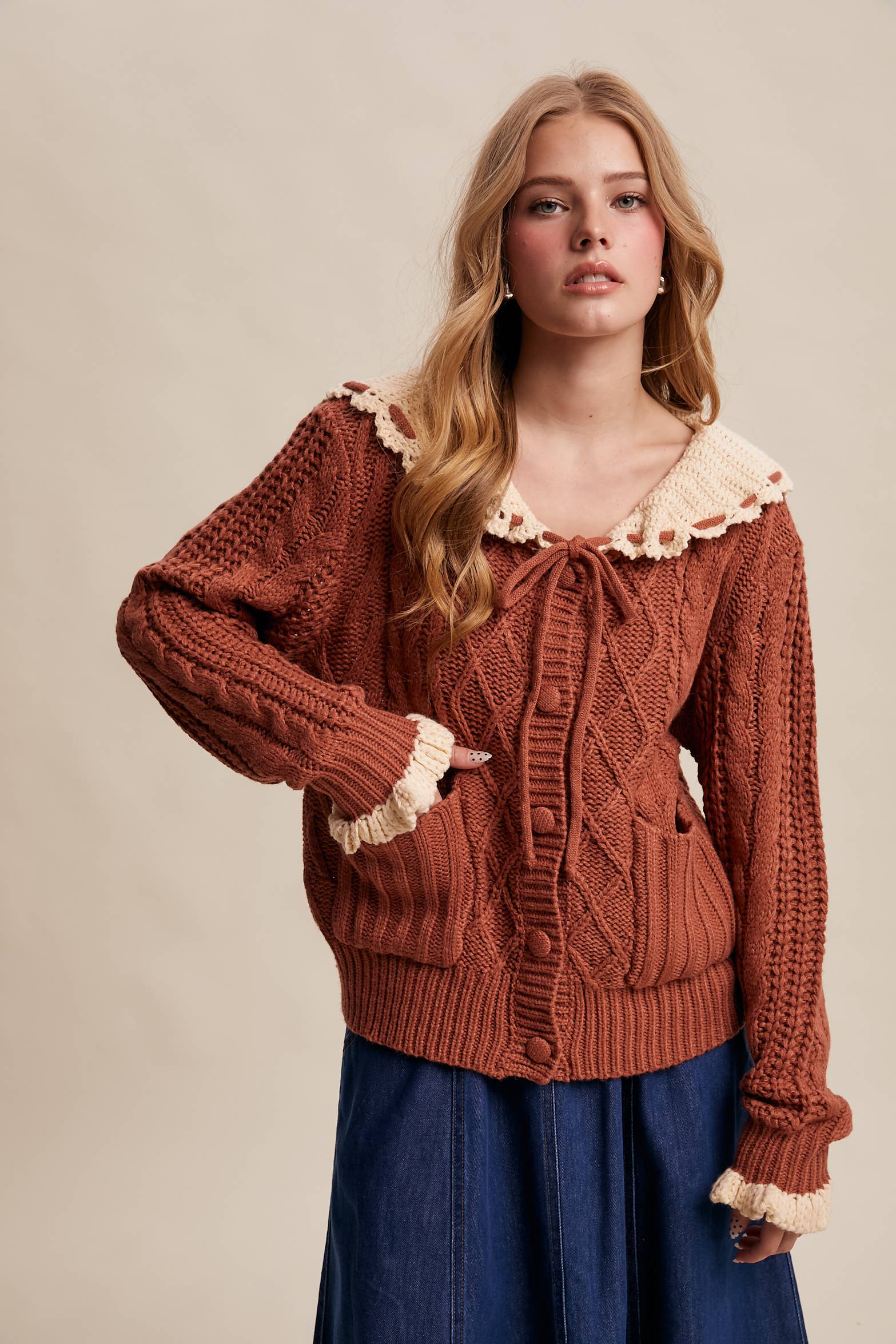Woman wearing a brown knitted cardigan with lace trim on a beige background