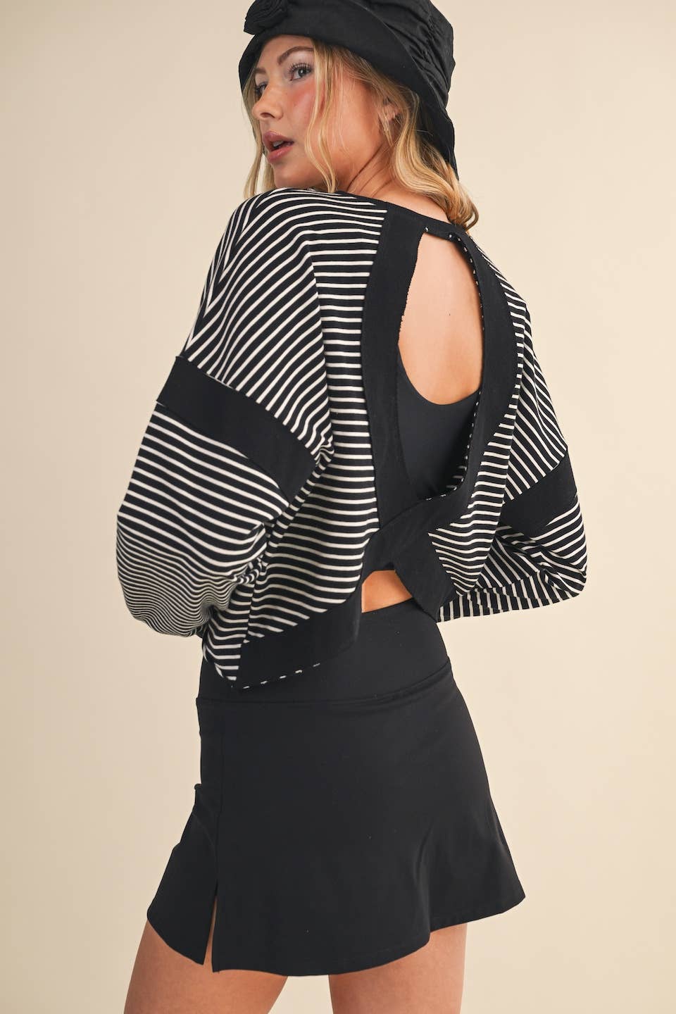 Woman wearing a black and white striped top with cut-out design and a black skirt on a beige background