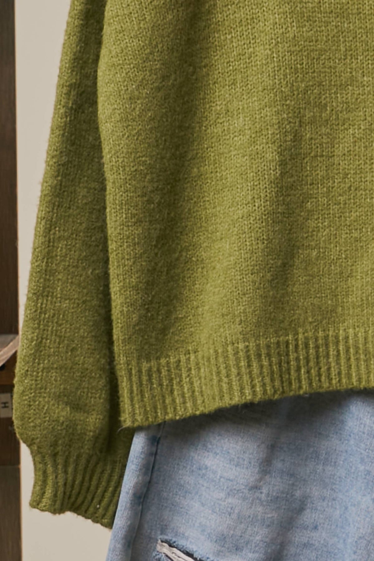Close-up of a textured olive green knit sweater draped over light blue denim jeans.