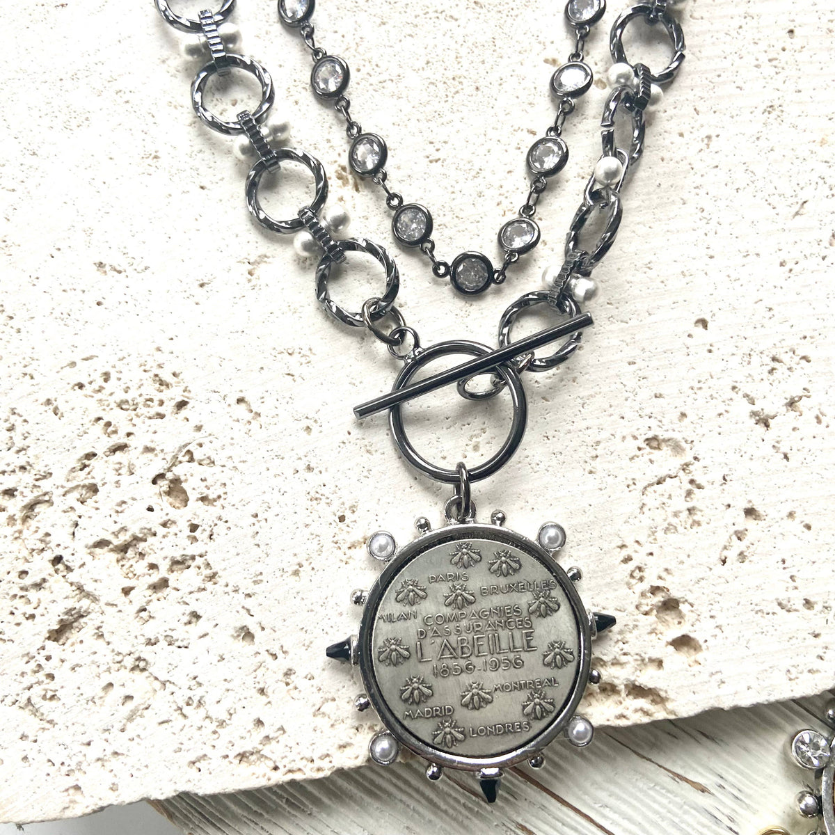 he Gunmetal Clear Crystal Layering Boutique Necklace pairs luminous clear crystals with a gunmetal finish displayed with a coin layering necklace 