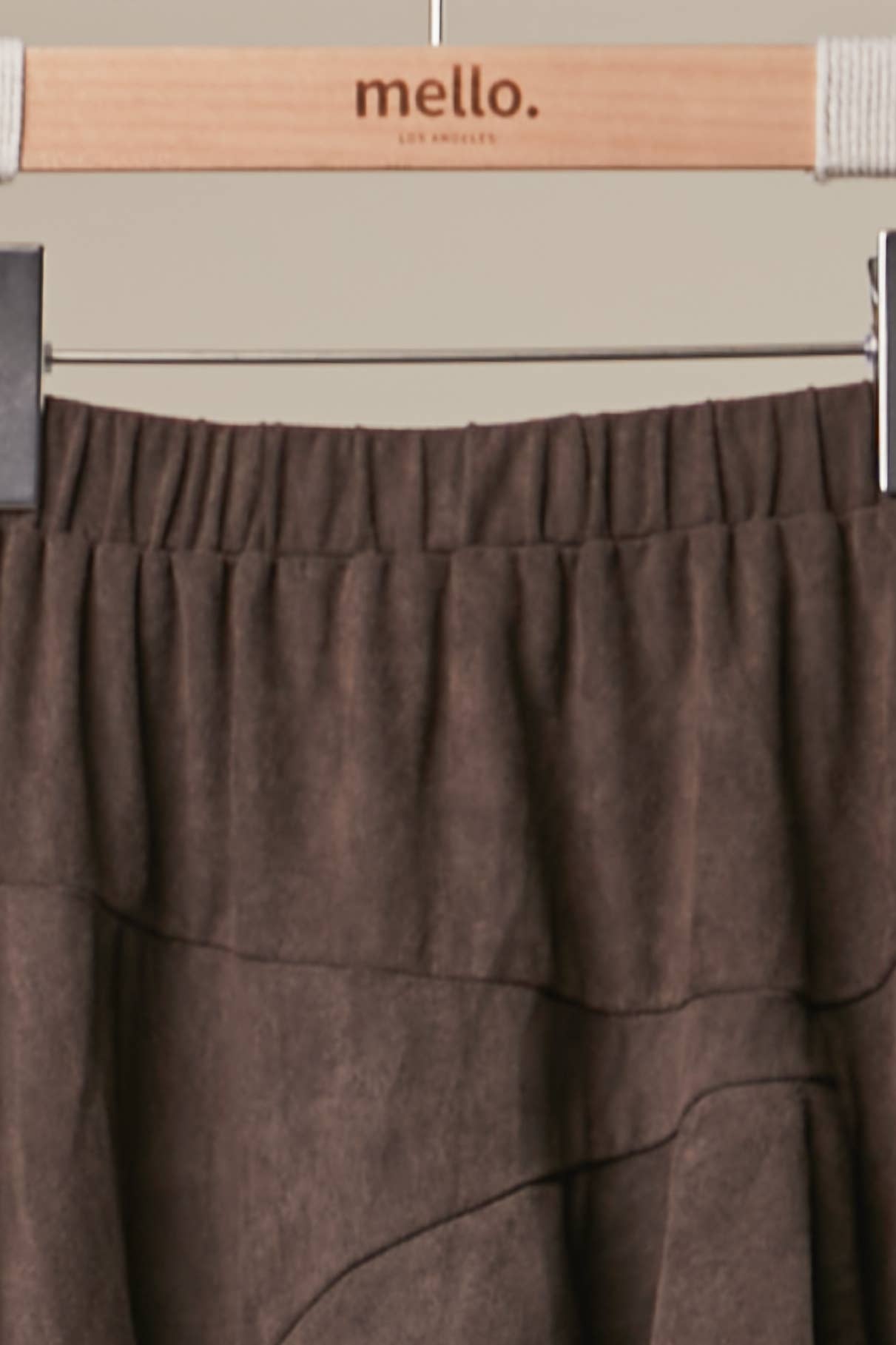 A close-up of a brown textured skirt hanging on a wooden hanger branded 'mello. LA MODELO'.