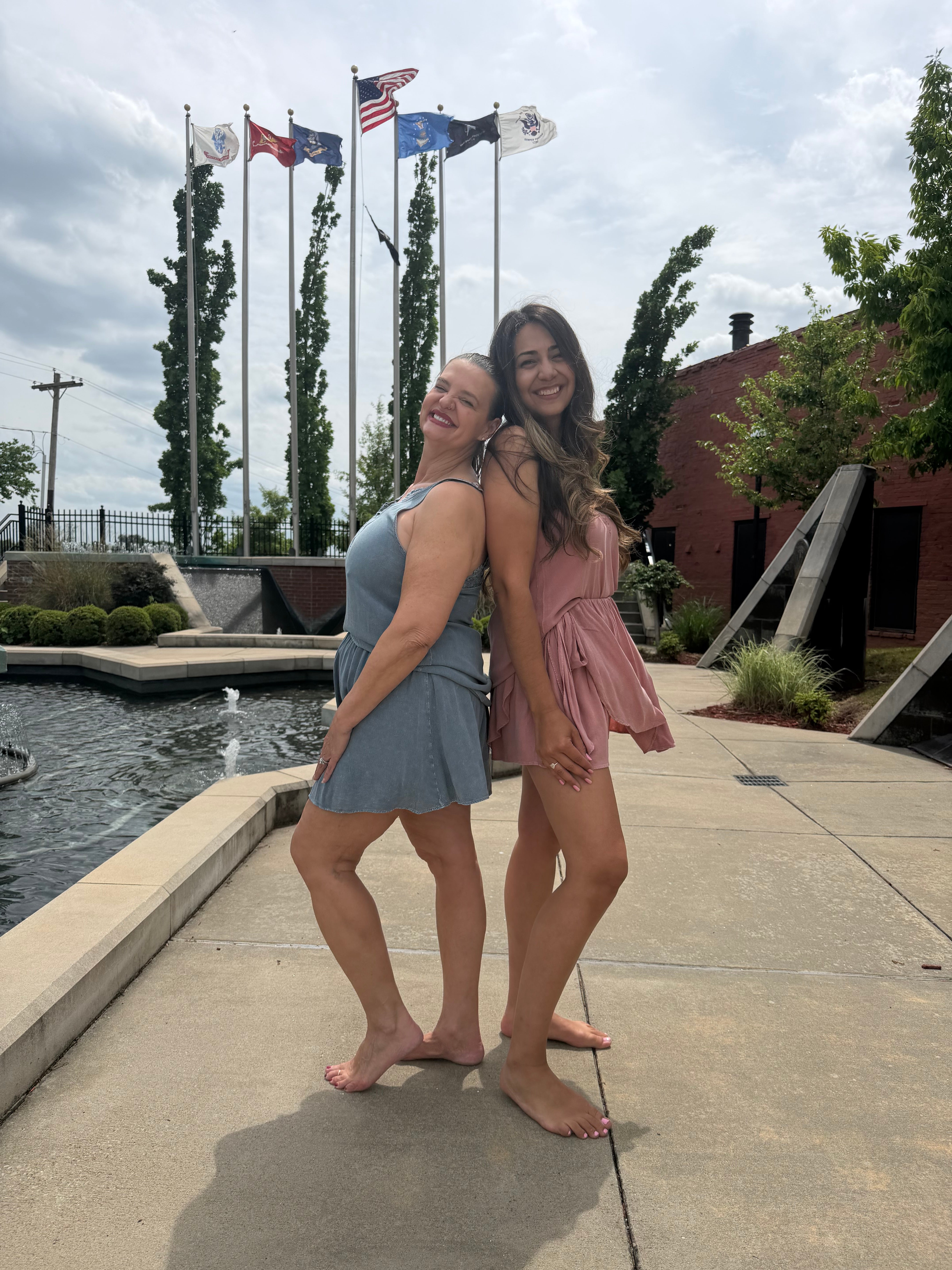 Two people posing on a sidewalk with flags and trees in the background