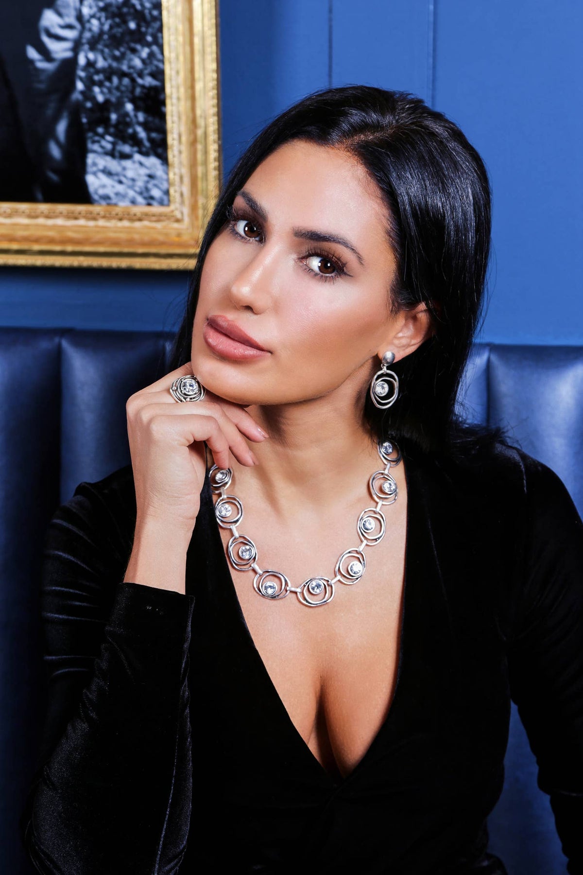 Woman wearing a silver necklace in a room with a blue wall and framed picture.