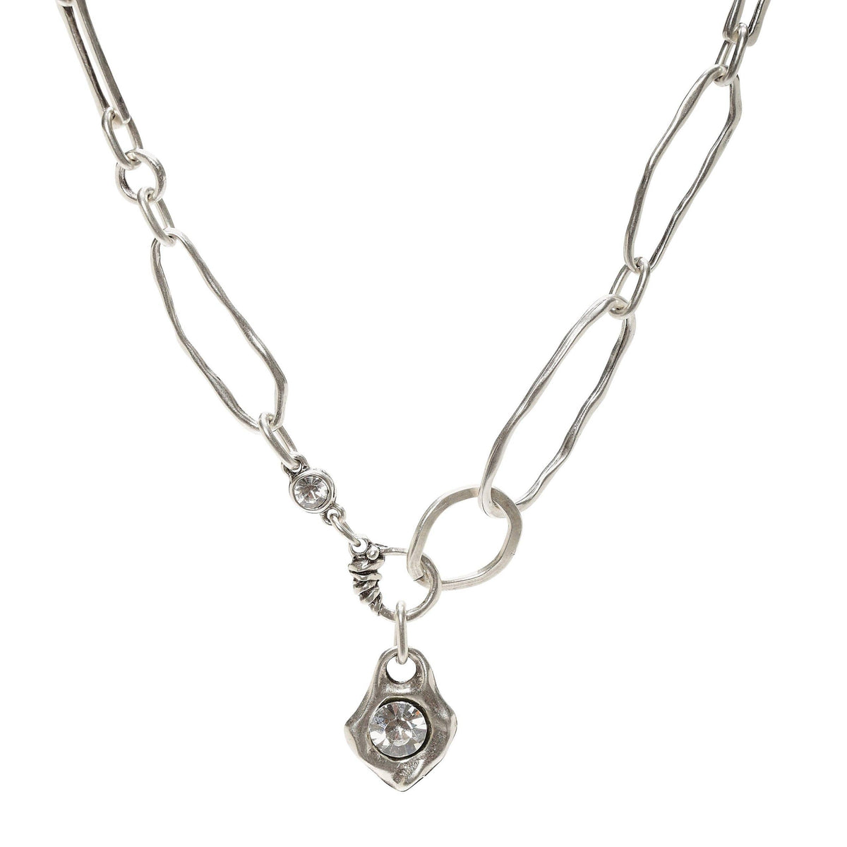 A silver paperclip chain necklace with a small textured charm and a dangling shield-shaped charm set with a clear round gemstone, shown on a plain white background.