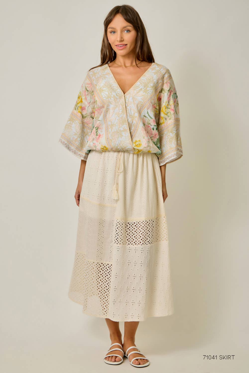 Woman wearing a floral blouse and lace skirt on a plain background