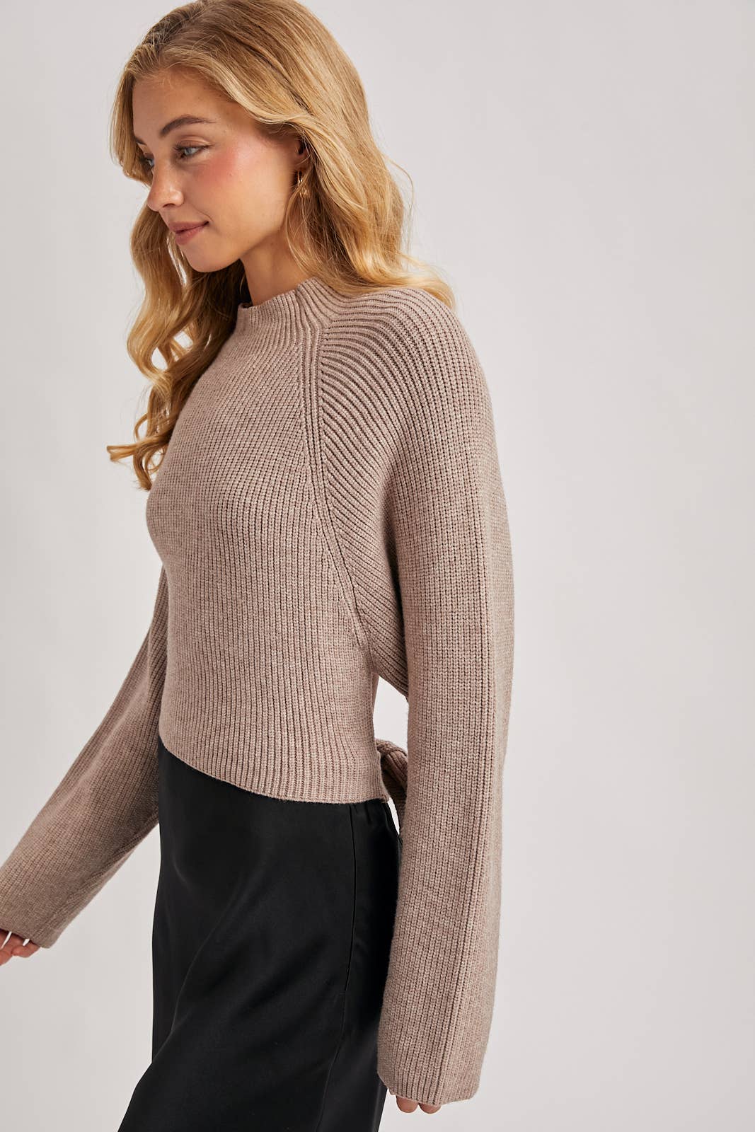 Taupe ribbed mock-neck sweater with wide long sleeves and a cropped fit, styled with a black skirt.