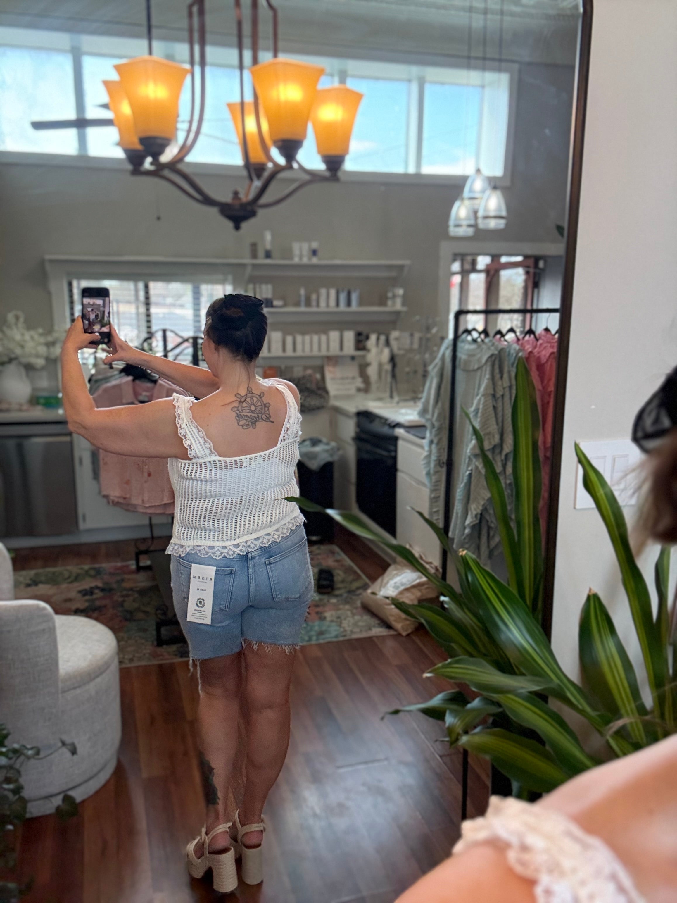 Person taking a mirror selfie in a kitchen, wearing a white top and denim shorts.