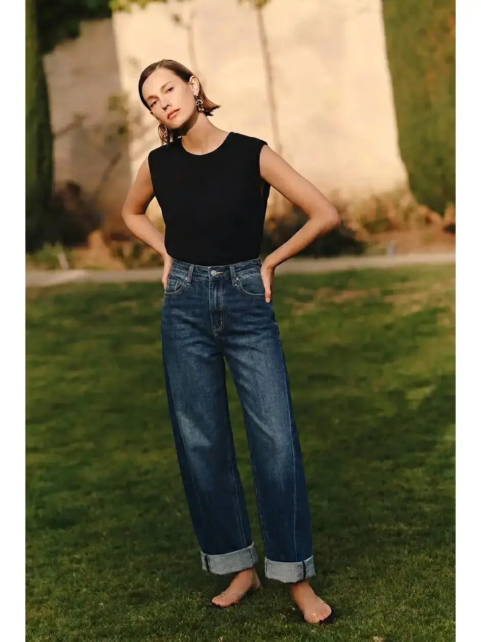 Woman wearing a black top and blue jeans standing on grass with a blurred background
