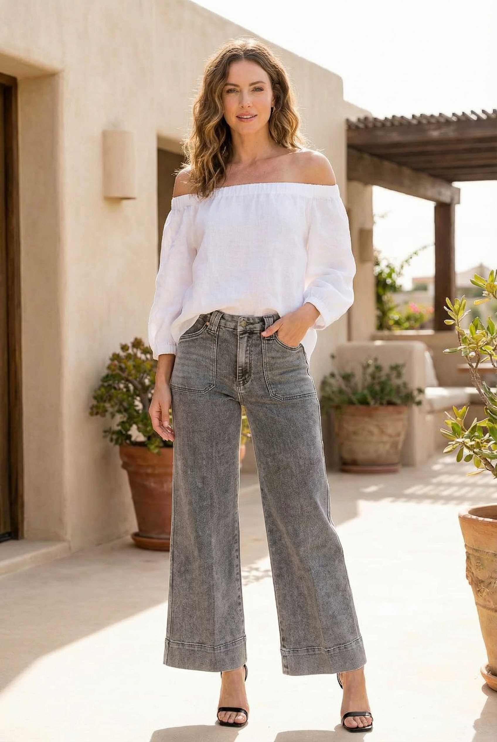 Woman wearing a white off-shoulder top and gray wide-leg jeans standing outdoors.