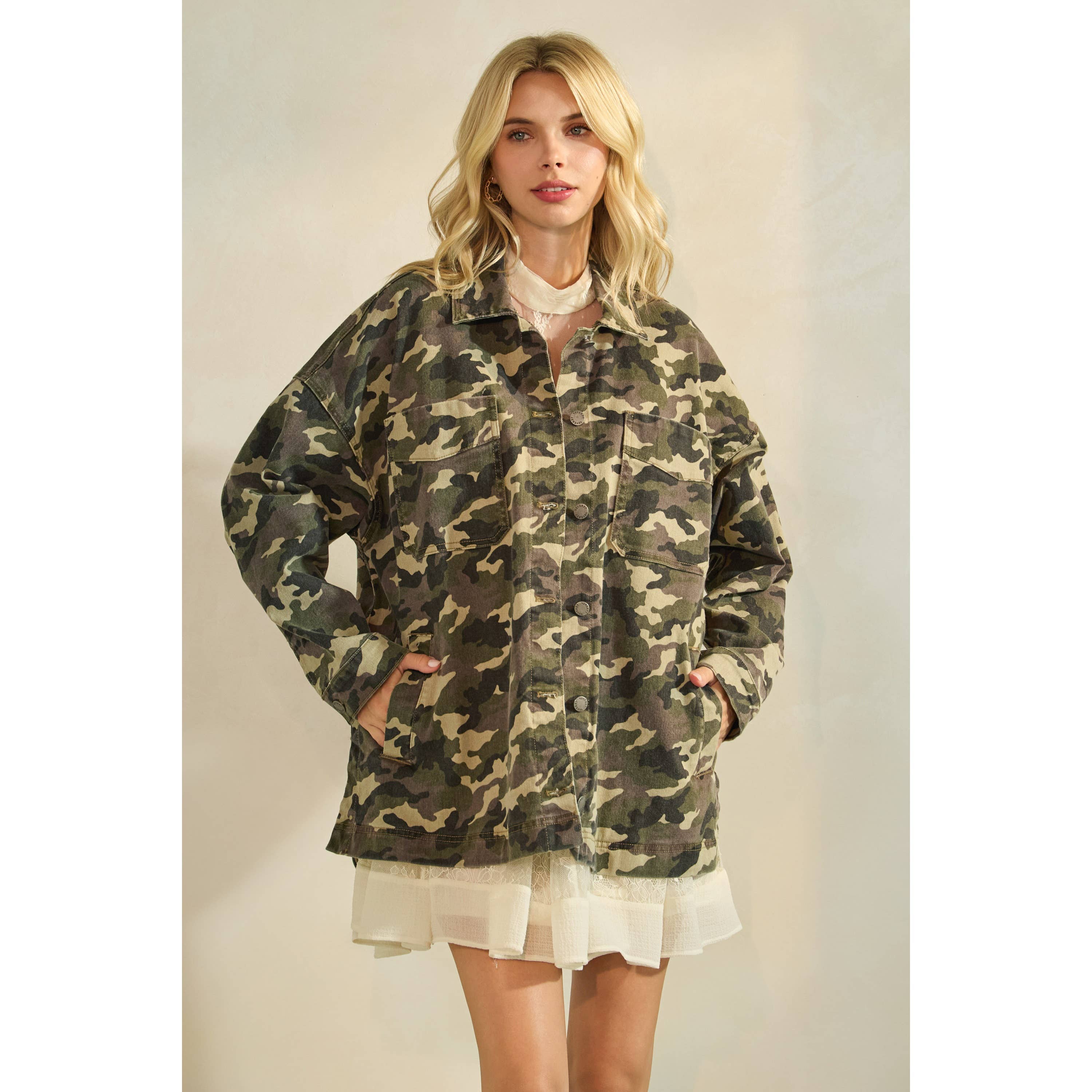 Oversized camouflage print jacket with front pockets and button closure, styled over a white tiered mini dress.