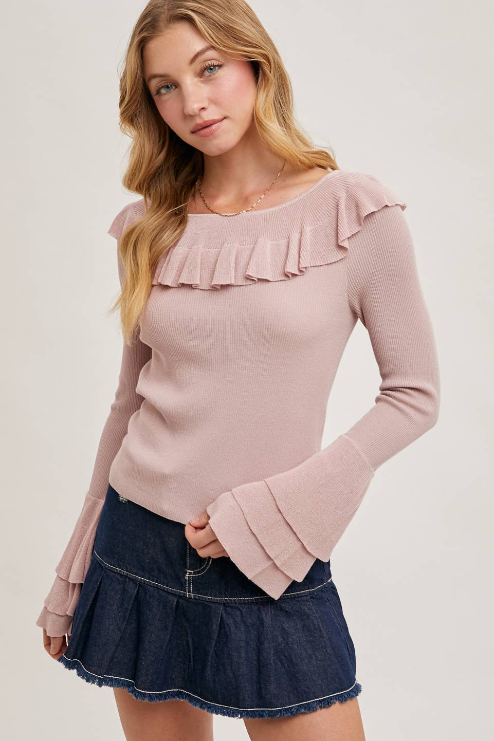 Beige ribbed knit sweater with ruffle neckline and tiered bell sleeves, styled with distressed denim shorts and a brown belt.
