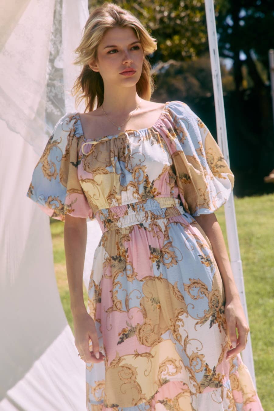 Woman wearing a patterned dress standing outdoors with greenery in the background