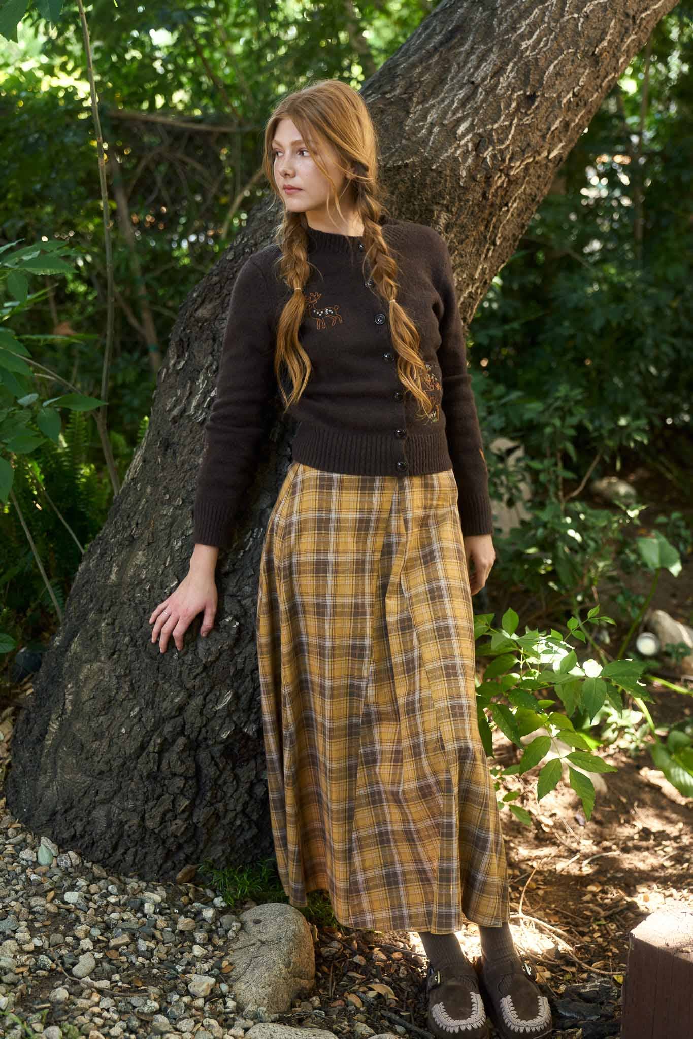 Woman in a black sweater and plaid skirt standing in a forest setting